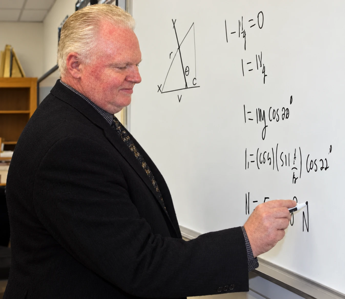 Mathematics teacher working through equations and a diagram on a classroom whiteboard
