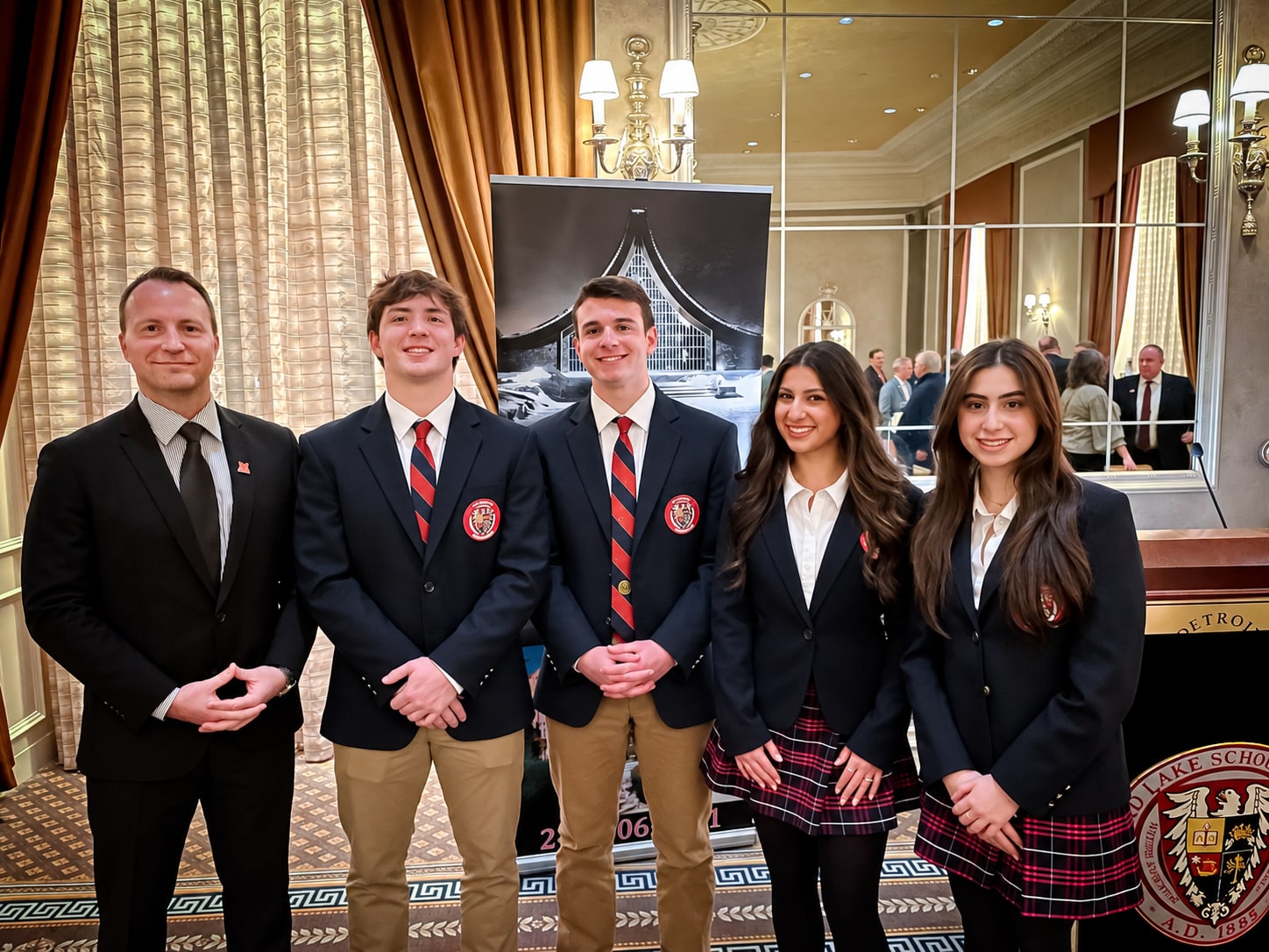 Four students in school uniforms standing with an adult at an alumni scholarship event