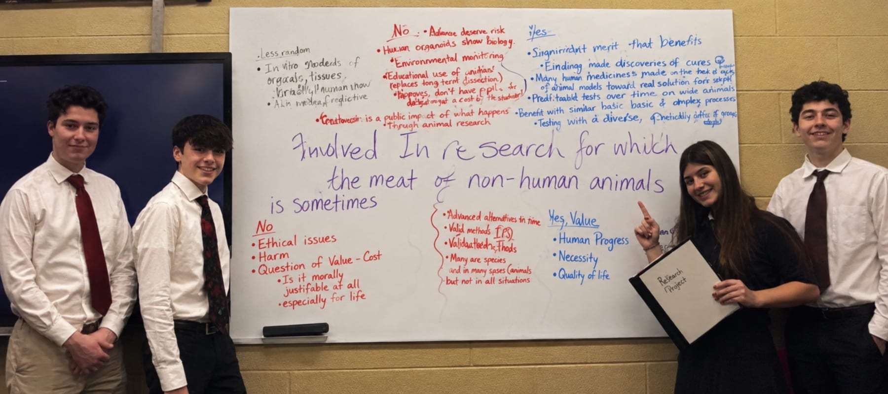 Students standing beside their research notes on a classroom whiteboard
